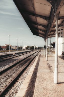 Issız bir tren istasyonunun dikey görüntüsü. Mesafe boyunca uzanan boş tren rayları. Metal destek kolonları ile kaplı bir sığınak. Açık bir gökyüzü altında sakin kentsel çevreler