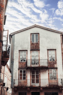 Santiago de Compostela, İspanya 'da üç katlı bir binanın dış cephesinin dikey çekimi. Beyaz boyası, kırsal balkonları ve dikey perdelerle süslenmiş klasik pencereleri var. Tarihi cazibe