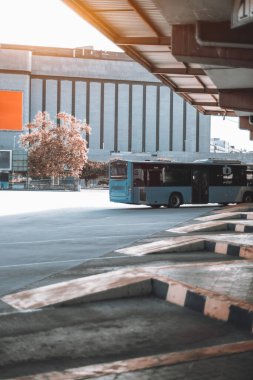 Metal çatının altına park edilmiş mavi bir otobüsle modern bir şehir otobüs durağının dikey görüntüsü. Beton platformlar turuncu ve siyah çizgilerle işaretlenmiş. Coruna, İspanya