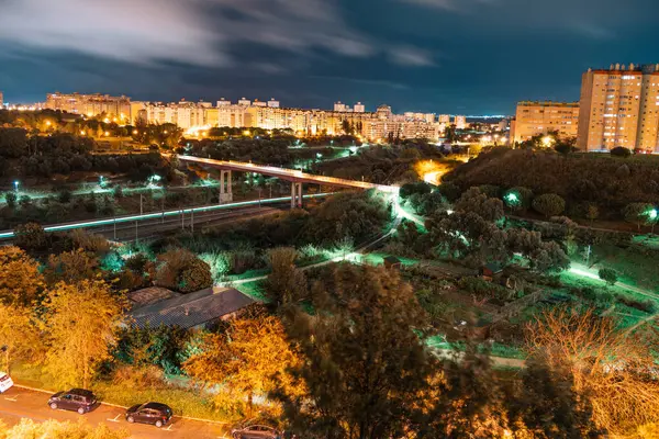 Lizbon, Portekiz 'deki Areeiro yerleşim bölgesinin hava gece görüşü. Apartman binaları, sokak lambaları, yeşil alanlar ve modern bir yaya köprüsü ile aydınlatılmış şehir manzarası.
