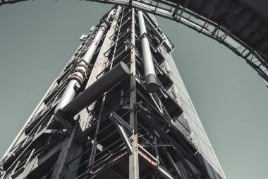 Çelik iskeleti, büyük metal boruları ve paslanmış yapısal detayları olan modern endüstriyel yüksek binalar. Düşük açılı görünüm yükseklik ve mühendislik tasarımı vurguluyor