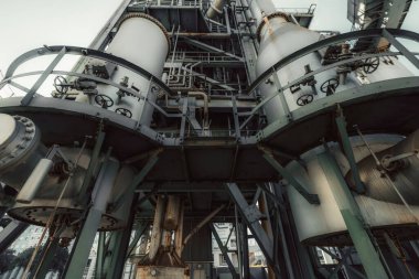 Çelik yapılar, borular, valfler, tanklar, ağır ekipmanlar ve düşük açılı geniş açılı mercekli karmaşık metal iskeletlerden oluşan büyük bir kimya veya imalat fabrikasının endüstriyel görünümü
