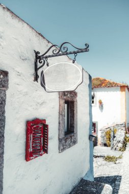 Aldeia da Mata Pequena 'da beyazlatılmış bir duvarda süslü bir demirden yapılmış boş bir levhaya asılı boş bir vintage mağaza tabelası. Aldeia da Mata Pequena' da, altında kırsal pencere ve kırmızı kepenk bulunan yazı veya logo için mükemmel bir model alanı.