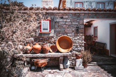 Aldeia da Mata Pequena 'da geleneksel taş avlusu granit bir masa üzerinde kırsal terracotta çömleği, kırmızı çerçeveli pencereler, kil çatı fayansları ve yumuşak gün ışığı altında klasik cazibe
