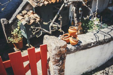 Aldeia da Mata Pequena 'nın taşralı avlusunun köşesinde yıpranmış taş bir duvarda bir yığın terracotta çömleği, kırmızı ahşap bir kapı, çiçek açan dallar ve büyüleyici kırsal mimari
