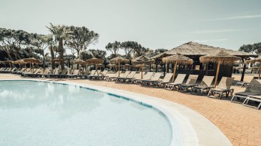 Punta Umbria, İspanya 'da güneş pansiyonları, saman şemsiyeleri ve yemyeşil Akdeniz ağaçlarıyla çevrili güneşli gökyüzünün altında sazdan yapılmış bir plaj barı olan Idyllic tropikal tatil beldesi.