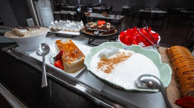 Çeşit çeşit tatlı büfesi, turta, krem şanti, sütlaç, kırmızı jelatin, çikolatalı pasta, hamur işleri, taze çilek ve servis kaşıkları dahil olmak üzere çeşitli tatlılar.