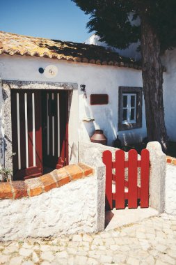 Aldeia da Mata Pequena 'daki geleneksel Portekiz kır evi, beyazlatılmış duvarlar, kırmızı ahşap kapı, kırsal kiremitli çatı ve sıcak öğleden sonra gün ışığında kaldırım taşı yolu