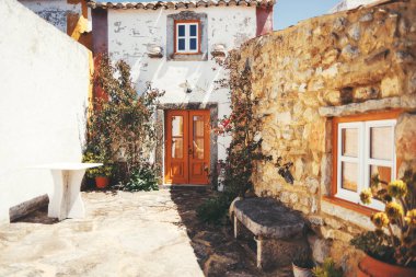 Portekiz 'in Aldeia da Mata Pequena kentindeki güneşli avluda canlı turuncu ahşap kapısı, taş duvarları, tırmanma tesisleri ve rahat dekoratif unsurları olan kırsal beyazlatılmış bir ev bulunuyor.