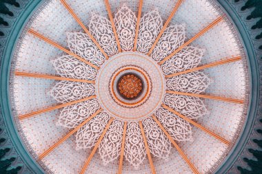 Çapraz simetriyle karışık İslami kubbe tavanı, ayrıntılı arabesk çiçek desenleri, ve altın süsleme aksanları, doğrudan yumuşak pastel ışıkta yakalanmış.