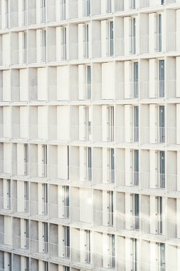 Tekrarlanan balkonları, temiz beyaz korkulukları ve sürgülü cam kapıları olan modern bir apartman veya otel cephesinin dikey telefon görüntüsü minimalist geometrik bir mimari desen yaratıyor.