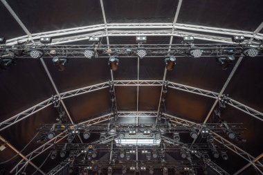 Profesyonel konser ışıklandırmasının detaylı görüntüsü, birden fazla askıya alınmış LED spot ışıkları ve siyah bir tepe örtüsü altında hareket eden başlıklar, açık hava gösterisi için hazır.