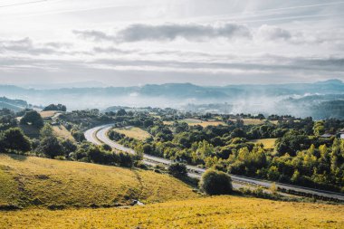 Asturias 'ta sonbahar manzarası yuvarlanan yeşil ve altın tepeler boyunca dolambaçlı bir yol vadide sabah sisi ve dramatik bulutlu gökyüzünün altında dağlar.