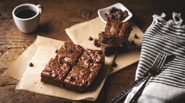  Çikolata parçalı brovniler, kahve ve çikolata parçacıkları, çatal ve bıçakla ahşap bir tahta ve biraz da kağıt..