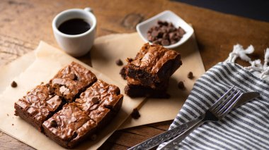  Çikolata parçalı brovniler, kahve ve çikolata parçacıkları, çatal ve bıçakla ahşap bir tahta ve biraz da kağıt..