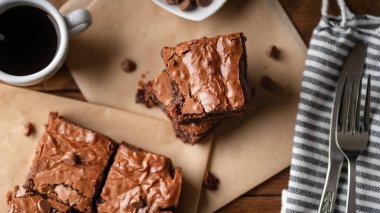  Çikolata parçalı brovniler, kahve ve çikolata parçacıkları, çatal ve bıçakla ahşap bir tahta ve biraz da kağıt..