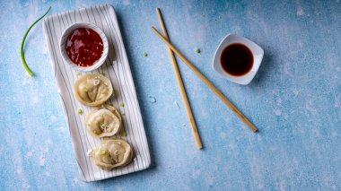  Tatlı ve baharatlı sosla servis edilen hamur köftelerine soya sosu ve mavi desenli arka planda seramik bir tabakta servis edilen çubuklar eşlik ediyor..