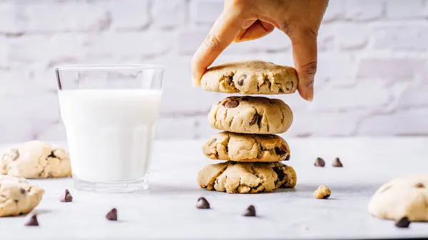 a person reaching for a cookie next to a glass of milk