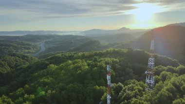  Altın saat boyunca yeşil ormanlarla kaplı tepenin tepesindeki 4G ve 5G Telekom Kulesi 'nin hava görüntüsü.