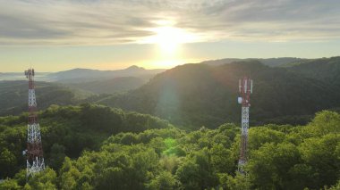 İnternet kablosuz akıllı telefon üretimi için 5G telekom kulesi anteninin hava görüntüsü. Dağ manzarasında destansı bir gündoğumu sırasında yeşil bir ormanın ortasında insansız hava aracı çekimi.