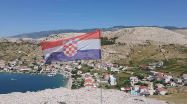 Adriyatik Denizi üzerinde kayalık bir kayanın üzerinde Hırvat bayrağı ve arka planda tipik bir geleneksel köy var. Hırvatistan 'da yaz tatilleri