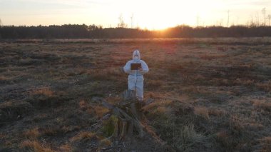 Maske ve tabletle harap olmuş açık havada koruyucu giysi giyen bilim adamları yıkıcı olaylardan sonra kirlenmiş toprak hakkında bilgi topluyorlar.