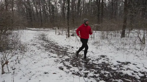 stock image Young Caucasian man in red shirt running through forest during winter time while snowing