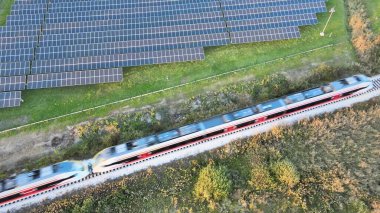 Modern elektrikli tren güneş paneli çiftliğinin yanında seyahat ediyor. Hava görünümü