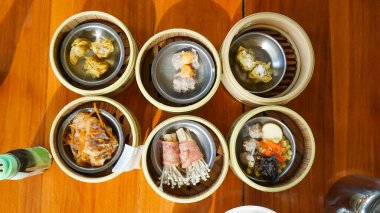 Ahşap masada Dim Sum, üst manzara, buharlı bambu sepetlerinde servis edilen Dim Sum 'un üst görüntüsü, Çin mutfağı.