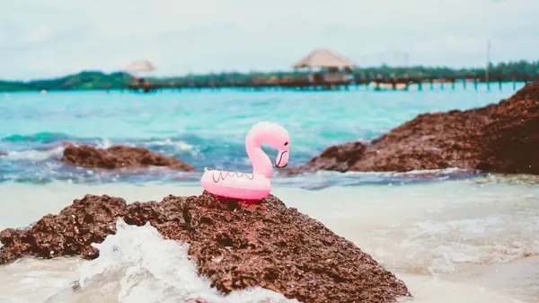 Small Pink rubber life ring on the beach. A swim ring in the shape of a pink flamingo, on the sand of a beach, with the ocean in the background.