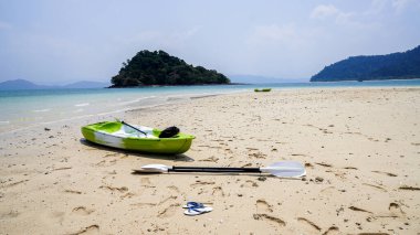 Sahil şeridi boyunca, renkli kanolar ön planda kürek ve sandaletler, Ulusal Park, Ranong, Tayland. Doğal Beyaz Kum Sahili. Aktif dinlenme, spor, kano. Suyun üstünde rafting yapmak için bir tekne. Kumsalda birkaç kano duruyor..