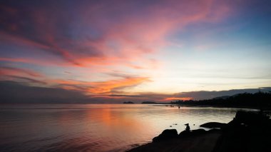 Tayland 'da gün batımında plaj. Birçok insan gün batımında plajda faaliyet gösterir. Önlerinde ve okyanusun üzerinde güneşin batışını izliyorlar. Sahilde gün batımında siluetler.