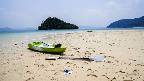 View along the shoreline, colourful kayaks paddle and sandals in foreground, National Park, Ranong, Thailand. Natural White Sand Beach. Active rest, sport, kayak. Boat for rafting on water. A few kayaks stand on a sandy beach.