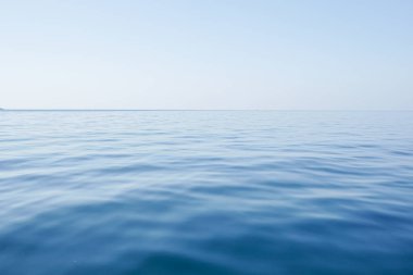 Gün ışığında sakin deniz yüzeyinin yatay çizgisi. Mavi gökyüzü arka planında deniz. Sabahın erken saatlerinde açık gökyüzünün altında deniz manzarası.