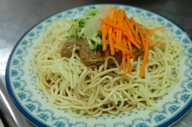 Tahta masadaki kasede etli şehriye. Geleneksel Tayvan mutfağından bir kase kurutulmuş erişte. Erişteler arpacık soğanı ve yeşil sebzelerle servis ediliyor..