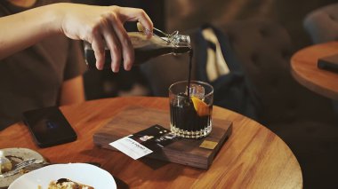 Portakal suyuyla soğuk kahve hazırlıyorum. Şişeden viski bardağına soğuk kahve dolduran bir el. Portakal suyu soğuk kahve. Seçici odak.