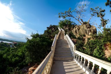 Gün batımında tepeye çıkan uzun merdivenler. Merdivenler dağın tepesine doğru gidiyor. Merdivenler yüksekliğe çıkıyor. Merdivenler mavi gökyüzüne ve güneşe karşı yokuş yukarı.