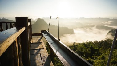 Dağ tepelerindeki bulutların tepesinde dağ zirveleri arasında akan sis. Kayalık kayalıkların arasında bulutlar sürükleniyor. Bulutların tepesinden bir dağın resmi. Dağ vadisinin üst manzarası Alçak bulutlarda gün doğumu