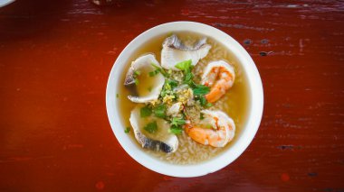 Balık ve karidesli pirinç lapası. Deniz ürünleri lapası, dilimlenmiş balık kalamarlı haşlanmış pirinç çorbası ve beyaz kasede karides. Asya usulü kahvaltı. Yulaf lapası ya da deniz mahsullü haşlanmış pirinç çorbası..