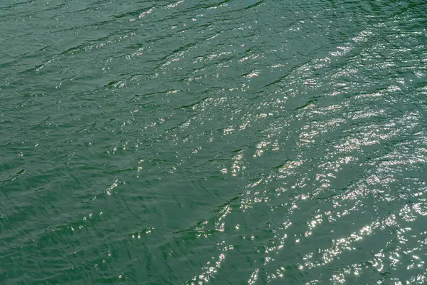 River from above, ocean water surface aerial view, water texture background, light blue green reflection on lake wave ripples flat surface. Sun light reflecting or sparkling glitter on water.