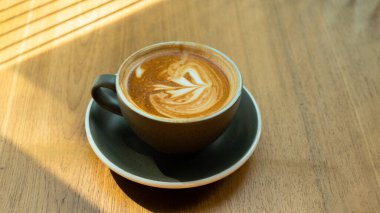 Ahşap masada geç kalmış kahve sanatı. Rahatlama konsepti. Süt köpüklü buzlu kahve ve güneş ışığı. Güneşli bir günde kahve / barda bir fincan sıcak kahve ve Croffle 'ın fotoğrafı..