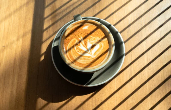 Late coffee art on the wooden table. relaxation concept. Iced coffee latte with soft white milk foam and sunlight shining through. Photograph of a cup of hot coffee and Croffle on table in a coffee/bar in during sunny day.