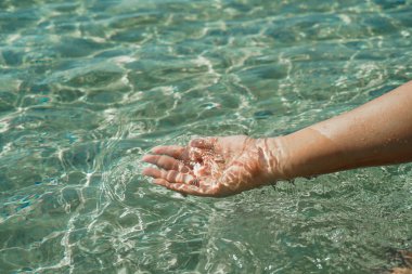 Saf suyla birlikte eller. Göl suyuna dokunan bir kadının eli. Bir insanın eli dalgalı bir su yüzeyine dokunmak için uzanır, duyusal algının dokunsal boyutunu keşfeder. Temizlik, doğa, çevre ve sürdürülebilir bir kavram.