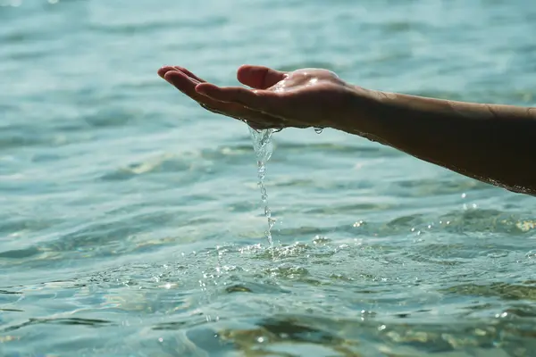Hands with pure water. Closeup of a woman\'s hand touching the lake water. A person\'s hand reaching out to touch a rippling water surface, exploring the tactile dimension of sensory perception. A concepts of cleansing, nature, environment and sustaina