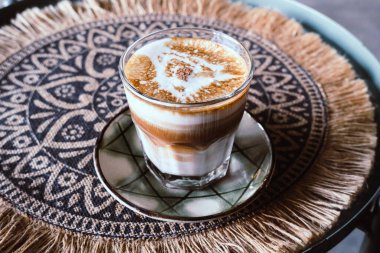 Süt katmanlı Latte cappuccino Macchiato Kahve, kızarmış kahve çekirdeği. Bir bardak kahve ve el dokuması kumaş arka planda güzel bir latte..