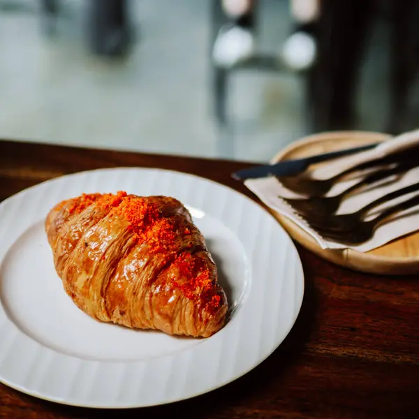 croissant , French croissant or French bread or custard croissant with icing sugar topping for serve. Fresh french croissant on white ceramic plate on bright light brown wooden table background