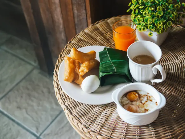 Breakfast food table scene Thailand style. Top down view over a rattan table background. Patongko, Sticky rice with pork wrapped in banana leaves, boiled eggs, soft-boiled eggs, coffee, orange juice.