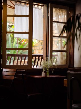 Çağdaş bir oturma odasının içinde şöminesi, beton ve koyu ahşap duvarları, beton zemini ve çatı katı pencereleri var. Kafenin oturduğu koltuğun penceresinden güneş parlıyor..