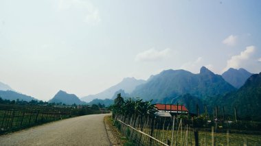 Arka planda kireçtaşı dağları olan çiftlikteki toprak yol, Vang Vieng, Laos. Laos 'un içindeki pirinç tarlalarının manzarası. Keskin dağ zirvelerinin önündeki yeşil tarlalar.