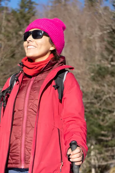 active woman dressed in pink winter clothes breathes fresh air in a forest, hiking route.